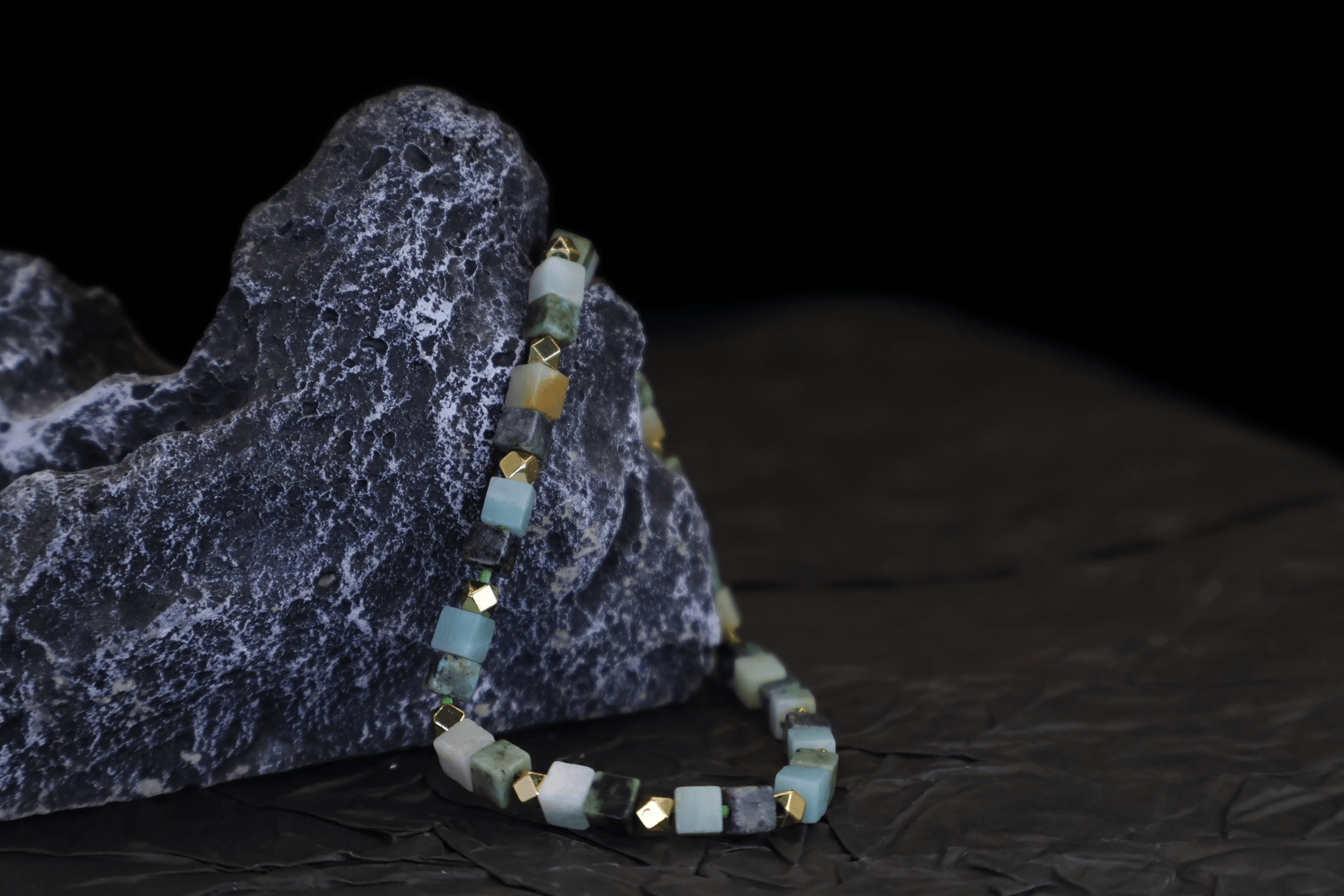 Grounding Multi-Green Amazonite Bracelet I with gold-plated sterling silver cubes draped over a textured dark rock