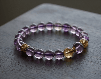 Natural Pure Amethyst & Tajing Bracelet I with Yellow Tajing and gold accents resting on a wooden table.