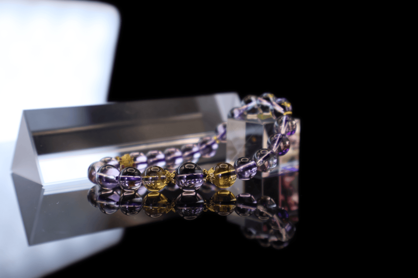 Elegant Pure Amethyst & Tajing Bracelet I styled on clear glass prisms against a black reflective backdrop.